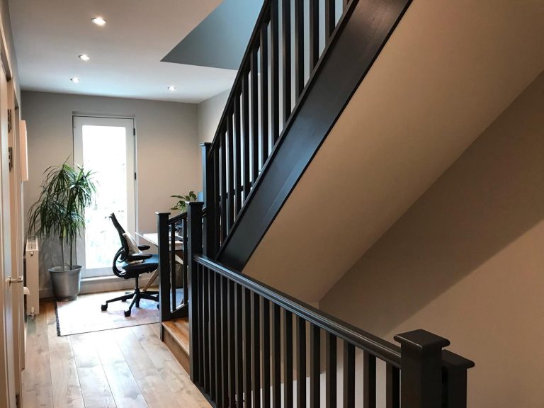 Interior of a hallway with a staircase, desk area, chair, and a potted plant.